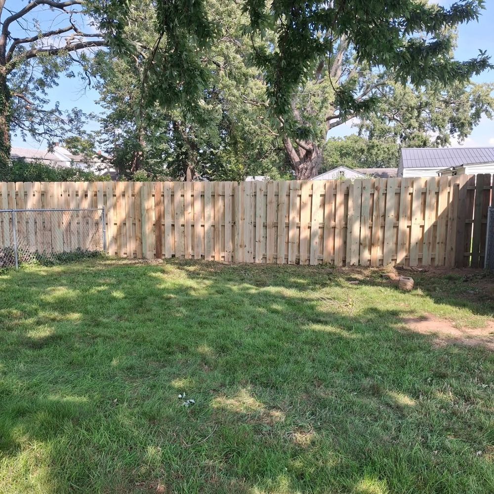 Wood fence along the back of a yard under big trees